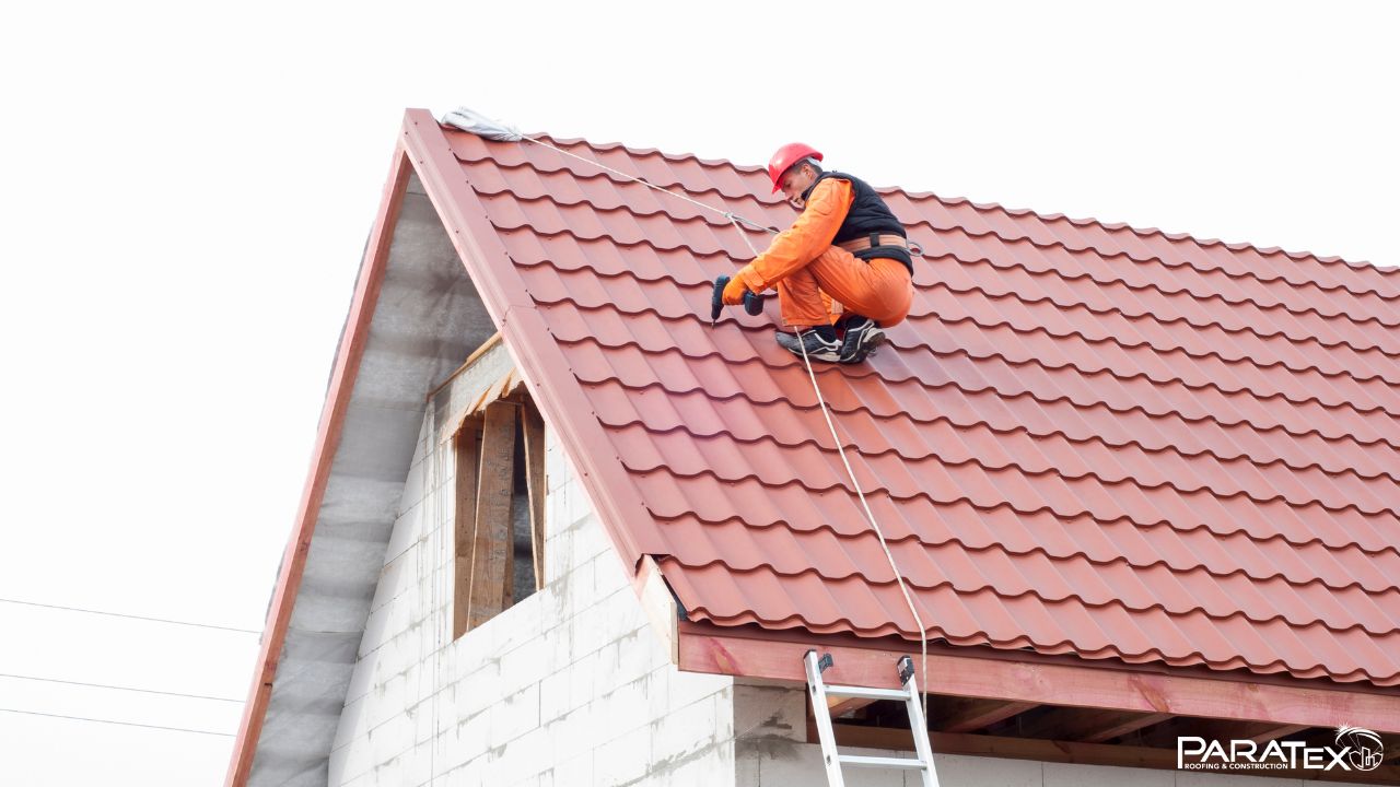 Construction worker on a red roof doing installation of the best roofing color for this property.